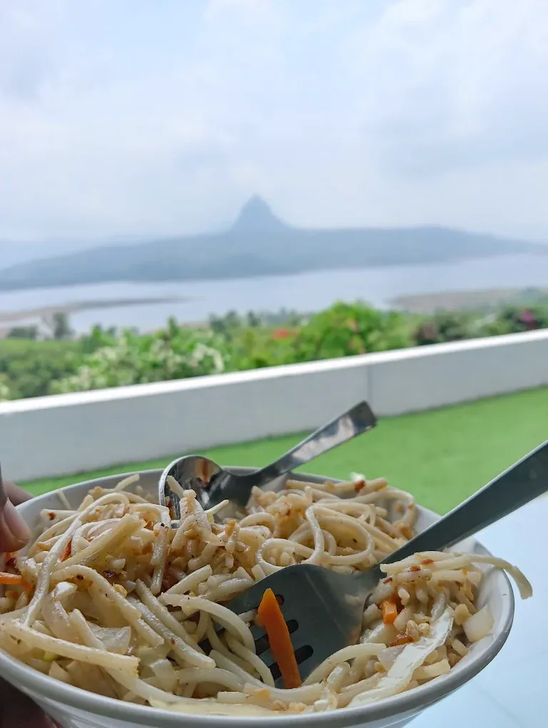 Plate of noodles with grass and Pawna Lake in the background